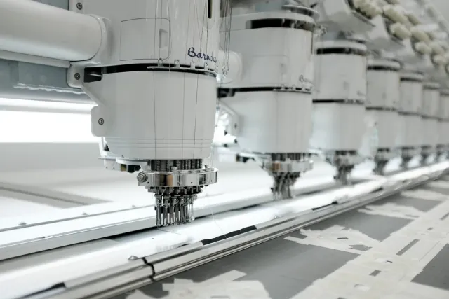 Row of embroidery machine heads, the nearest one close up with its needles