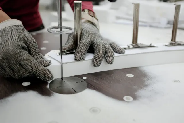 Worker in a steel-mesh glove guiding stacked fabric through a band knife