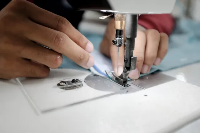 Hands guiding fabric under a sewing machine needle