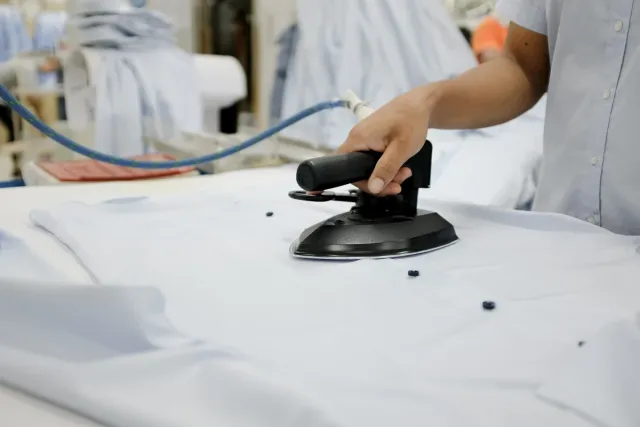 Worker pressing a finished light blue shirt